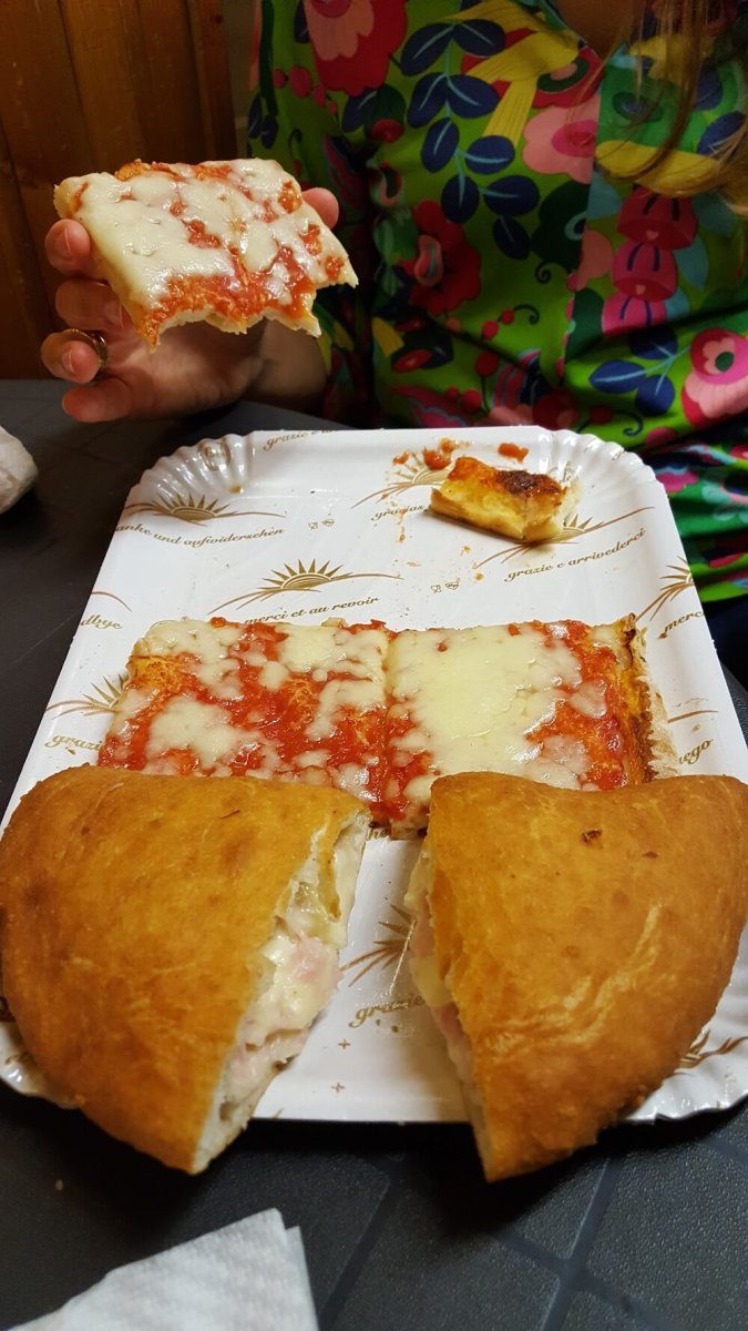 Un trancio di pizza tenuto in mano e un calzone fritto nel piatto.